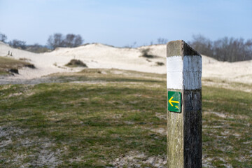Yellow arrow trail marker in grassy dunes – navigation sign in coastal landscape