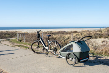 Electric bike with green child trailer parked on coastal dune with sea view