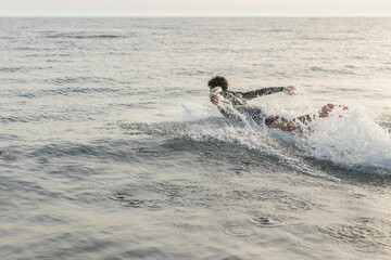 Surfer paddling on surfboard in ocean during sunset