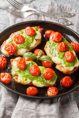 Margherita chicken that features pan-fried chicken breasts topped with melted mozzarella, pesto and tomatoes close-up on pan on table. Vertical