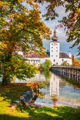 Schloss Ort, Austria surrounded by autumn-colored trees, reflects on Traunsee water.