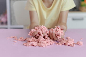 The kid plays with kinetic sand stirring it in her hands. Close-up view of children's hands with...
