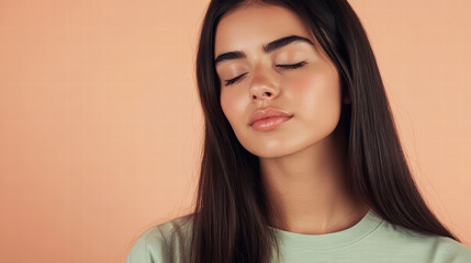 Fototapeta premium Peaceful Serenity: A young woman with long dark hair closes her eyes, radiating tranquility and inner peace against a soft peach background.