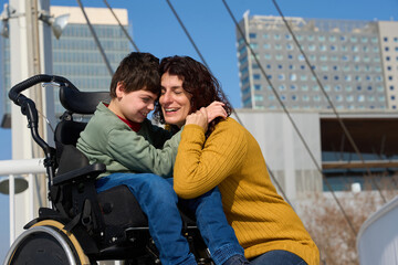 Happy mother hugging her son with cerebral palsy in wheelchair outdoors