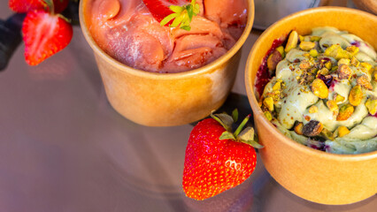 delicious ice cream in cardboard boxes with strawberry,pistachio and chocolate taste. to go dessert for refreshment in sunny summer days, slice of fresh fruits, nuts and grated chocolate as decoration