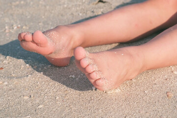 Sandy feet resting on the beach, capturing the essence of summer relaxation and enjoyment by the seaside. The image highlights the texture of the sand and the carefree feeling of a beach day.