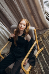 Obraz premium A beautiful blonde model, a young girl, a teenager in a studio in a black jacket and jeans in an armchair