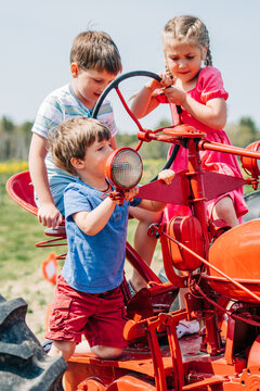 Three children playing on a red vintage tractor in a sunny field