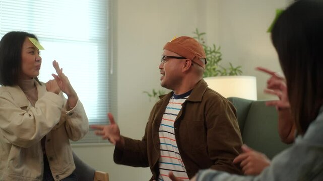 A group of young Asian friends is playing a fun charades game, guessing animal names at a lively home party on the couch. Laughter fills the room as they try to guess each other's clues.
