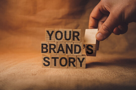 Wooden cubes spelling "Your Brand's Story" on burlap background, hand arranging cube, showcasing brand storytelling concept for business and marketing