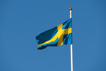 The national flag of Sweden with a yellow Nordic cross on a blue field flies high against a clear sky.
