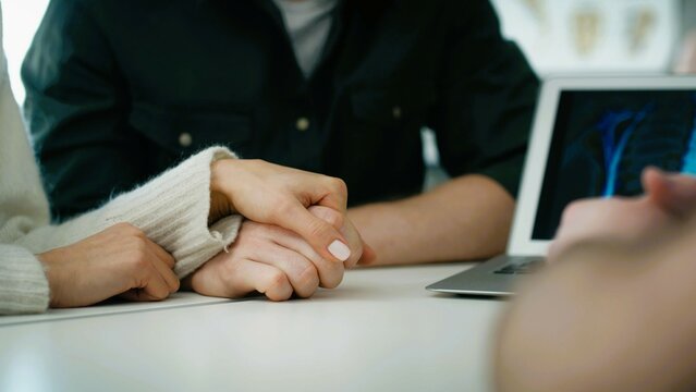 Doctor consulting young couple patients in fertility clinic about IVF or IUI. Doctor encourages and assures the young couple that everything will be fine..