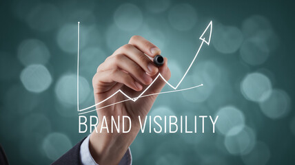 Hand drawing upward trending graph, indicating brand visibility growth on teal bokeh background, showcasing business success and marketing strategy