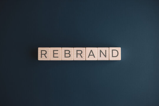 Wooden blocks spelling "REBRAND" on a dark blue background, showcasing a concept of business renewal or relaunch, ideal for marketing and advertising mockups