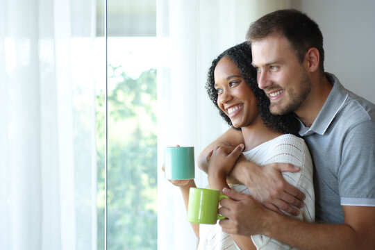 Happy interracial couple contemplating and drinking tea at home