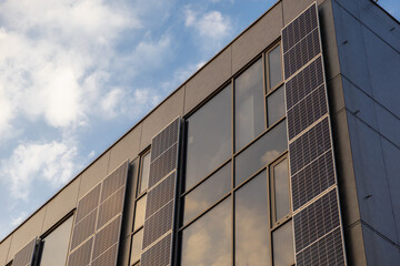 Fototapeta premium Modern building facade with vertical solar panels and large glass windows reflecting soft evening sky