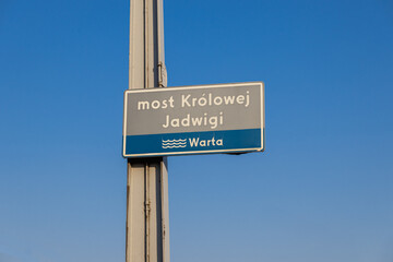 Fototapeta premium Queen Jadwiga bridge sign in Poznań with Warta river label against clear blue sky on a sunny day