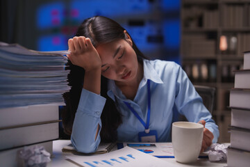 Young office worker sleeping at her desk during the night, feeling exhausted from long hours of...