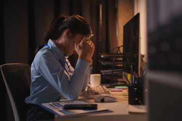 Young businesswoman suffering from headache while working late at night in office, massaging her...