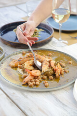 Young woman having dinne, eatiing prawns, r in the Mediterranean restaurant. Various dishes served on the table.	