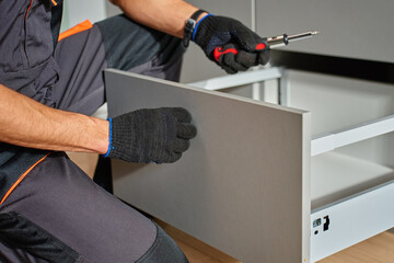 Man assembling kitchen drawer in modern cabinet using screwdriver. Handyman installing and...