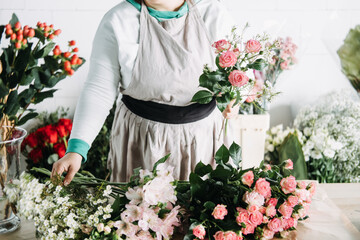 Florist arranges pink lilies and roses into a lush floral display on a studio worktable....