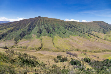 Obraz premium Majestic green mountain with natural ridges and a clear blue sky background. A breathtaking natural landscape perfect for travel, outdoor adventure, and nature conservation projects.