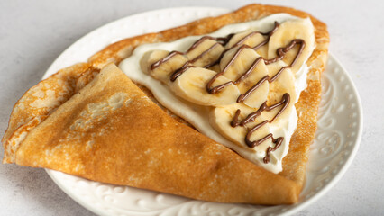 Crepes (thin pancakes, traditional russian dessert blini) with fresh berries, banana slices, melted chocolate and green mint. Maslenitsa concept.