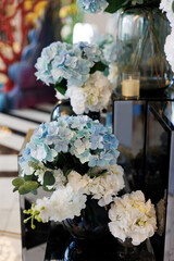 Wedding decoration. An elegant floral arrangement with blue and white hydrangeas in dark vases on mirrored pedestals creates a refined and modern atmosphere for the celebration.