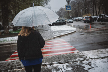 Woman under an umbrella in a heavy snowfall crosses the road at a crossroads. Bad weather, climate...