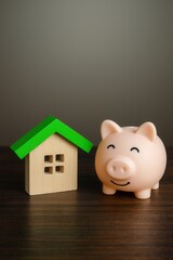 Wooden house model and piggy bank placed on wooden surface to symbolize savings and home investment