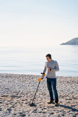 Beach cop sweeps a metal detector over a beach by the sea