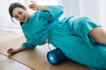 Woman rolling hips on a blue foam roller on cork mat at home. Myofascial release, body awareness,...