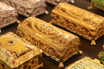 Ornate gold boxes with intricate designs displayed on a dark surface. The boxes showcase elaborate patterns and craftsmanship, emphasizing luxury and refinement. Perfect for decoration and gifting