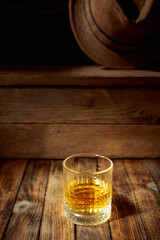 Elegant whiskey glass filled with amber liquid on a old wooden table.