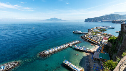 Obraz premium Sorrento, Italy – Stunning panoramic view from the Villa Comunale terrace. The port of Sorrento with its dramatic cliffs and turquoise sea stretches out toward Mount Vesuvius in the distance. 