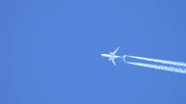 Flying jet plane leaving vapor trails in clear blue sky. Soaring aircraft producing contrails during high altitude flight. Cruising airliner generating condensation trails across bright sky