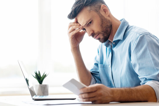 Concerned young businessman looking at smartphone working in office, waiting message, received bad sms with threat, using cellphone, touching forehead with thoughtful face expression, copy space