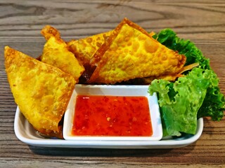 Deep fried pork wontons with sweet chilli sauce on wooden table.