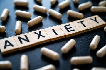 Word Anxiety composed with wooden alphabet on a black background, and around medicinal tablets. Care of anxiety.