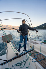 Young man captain standing at the helm and controls a sailboat during a journey by sea in winter time in Montenegro
