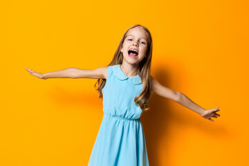 Joyful little girl in blue dress with outstretched arms against a vibrant orange background