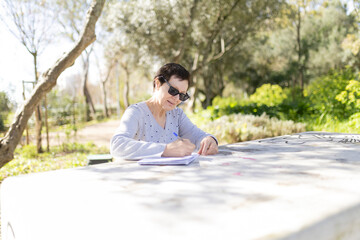 Fototapeta premium Senior woman writing outdoors in a sunny park