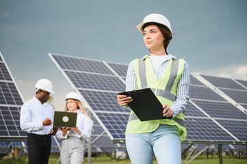 Portrait of young female engineer in special uniform standing near solar panels. Beautiful female...