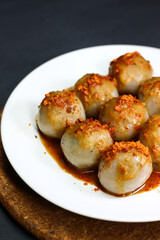 Cilok is a typical West Javanese food, made from tapioca flour and served with chilli sauce. It has a round shape like meatballs, isolated on a black background. Selective focus