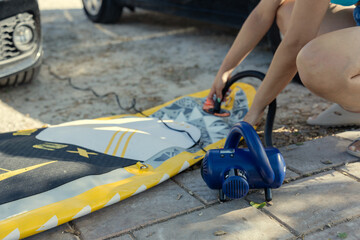Woman inflates her paddle board with an electric pump on a sunny day