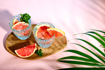 Refreshing chilled drinks with grapefruit and fresh mint in the bright rays of the sun under palm...