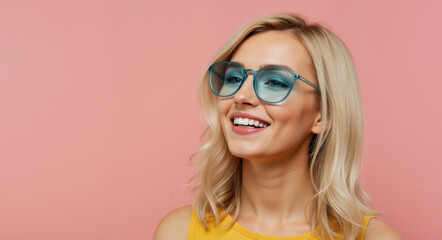 Smiling blonde woman with blue glasses against pink background wearing yellow top. Happy portrait with wavy hair and bright smile. Beauty concept for eyewear advertising