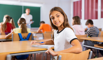 Schoolgirl sits half-turned at desk in classroom at a lesson in elementary school