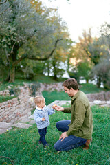 Fototapeta premium Dad hands a fruit to a little girl sitting on his knees in front of her on a green lawn